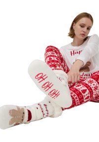 Czerwono-biała piżama świąteczna z wzorem pierniczków. Skarpetki mają czerwony napis "HO HO HO!" na białym puszystym materiale.