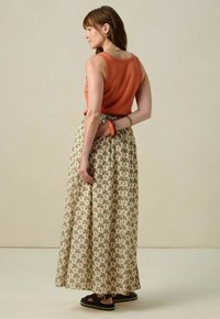 Haut sans manches orange, jupe longue à motifs avec un design de palmiers en vert et marron, associée à des sandales noires et un bracelet orange.
