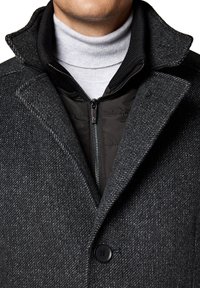 Szary płaszcz z wełny z domieszką, o teksturowanym wzorze jodełki, z czarną zapinaną na zamek wewnętrzną warstwą, kołnierzem oraz zapięciem na guziki.