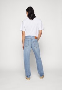 Ljust blå denimjeans med rak bendesign, med en brun läderpatch baktill och subtila sömnadsdetaljer, kombinerade med en vit t-shirt.