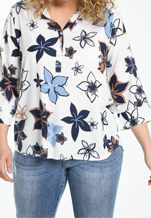 Hvid knapbluse med store marineblå, blå og brune blomsterprint, båret med blå denimjeans.