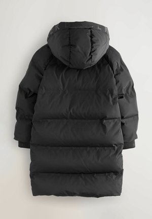 Doudoune noire avec capuche, présentant un design matelassé, une texture douce et des poignets élastiques contrastants. Détail du logo visible sur la capuche.