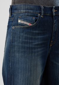 Tummansiniset farkut, joissa on slim fit -malli. Huomionarvoista on pieni etutasku, kuluneet kohdat ja kontrastiväriset ompeleet. Diesel-logon näkyminen.