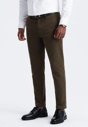 Chinos de un verde oliva oscuro con un corte ajustado, que cuentan con bolsillos laterales y una textura suave, combinados con zapatos de cuero negros.