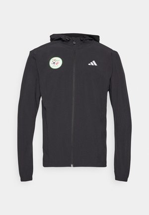 Zwarte hoodie met rits en een capuchon met trekkoord, voorzien van een ronde groene patch met een voetbaldesign en het witte Adidas-logo op de borst.