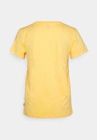 T-shirt jaune uni à manches courtes, vu de dos, avec un ourlet droit et une petite étiquette rouge en bas à gauche.