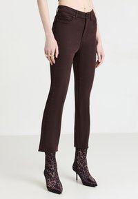 Jeans en denim marron avec une coupe slim, un ourlet effiloché et un design classique à cinq poches, associés à des bottines à imprimé léopard.