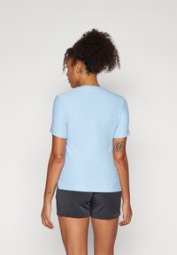 Haut à manches courtes bleu clair avec un motif à pois texturé, encolure arrondie et coupe ajustée, associé à un short gris foncé.