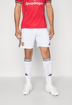 Maillot de football rouge avec des accents noirs et un logo, associé à un short blanc portant un emblème du club. Chaussettes blanches avec des rayures noires et crampons.