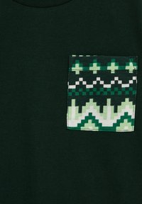 Tricou de culoare verde închis, cu un buzunar multicolor ce prezintă modele geometrice în nuanțe variate de verde, alb și negru. Textură netedă.