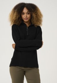 Schwarzer Pullover mit hohem Kragen und Viertelreißverschluss. Texturiertes Ripp-Gewebe, lange Ärmel, seitliche Schlitze und lockere Passform.