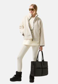 Biała kurtka z polaru z czarnymi wykończeniami, kremowy top, białe legginsy, czarna pikowana torba i czarne zimowe buty. Duże, przyciemniane okulary przeciwsłoneczne.