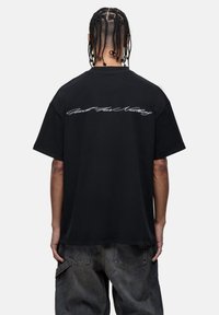 Black cotton t-shirt, short sleeves, loose fit. Features white cursive text "Good For Nothing" across the upper back. Textured fabric.