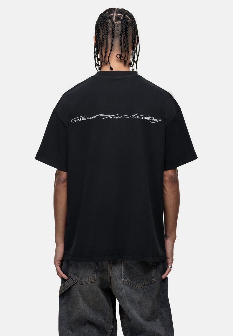 Black cotton t-shirt, short sleeves, loose fit. Features white cursive text "Good For Nothing" across the upper back. Textured fabric.