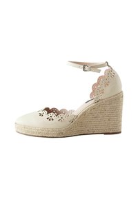 White leather wedge shoe with scalloped cutouts and floral perforations, featuring a jute-wrapped heel and ankle strap with buckle closure.