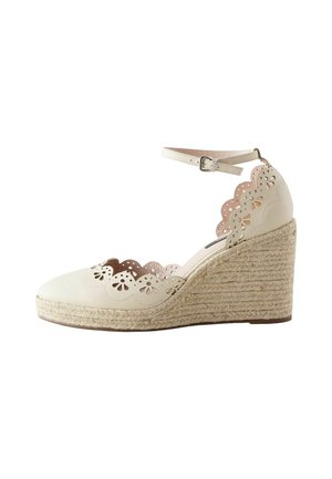 White leather wedge shoe with scalloped cutouts and floral perforations, featuring a jute-wrapped heel and ankle strap with buckle closure.