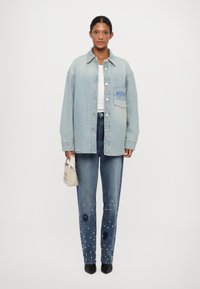 Lichtblauwe oversized denimjas met een zak aan de voorkant; gecombineerd met donkerblauwe jeans met witte versieringen en een aansluitende pasvorm.