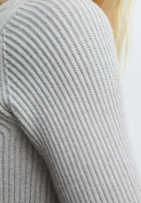 Šedý žebrovaný rukáv svetrů s texturovaným pleteným vzorem. Tkanina vypadá měkce a mírně elasticky, s přiléhavým střihem.