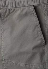 Gros plan d'une poche en tissu gris avec des coutures visibles et une ceinture élastique froncée en haut du pantalon.