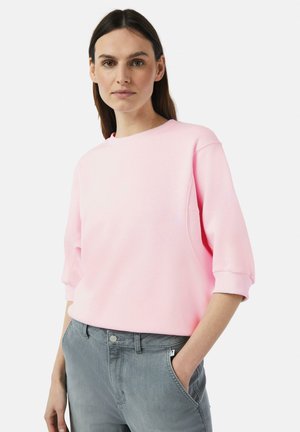 Roze oversized sweatshirt met een ronde halslijn en hangende schouders. Zachte stof en een relaxte pasvorm, gecombineerd met grijze spijkerbroek.