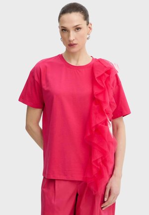 Donna che indossa una maglietta rosa acceso a maniche corte con dettaglio in tessuto arricciato che scende su un lato e pantaloni rosa coordinati.