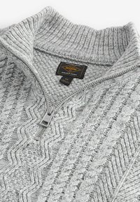 Jersey gris de punto con cremallera y un patrón texturizado de zigzag. Presenta un cuello alto y una cremallera de metal. La etiqueta indica tamaño M.