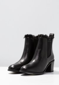 Botas de tobillo de cuero negro con paneles laterales elásticos, ribete de piel sintética, punta redonda y tacón cuadrado. Nombre de la marca visible en el costado.