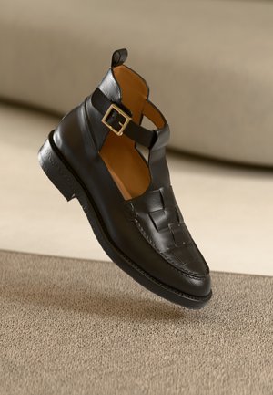 Chaussure en cuir noir avec motif tissé et détail de boucle dorée. Design à talon ouvert ; bout arrondi ; semelle texturée.