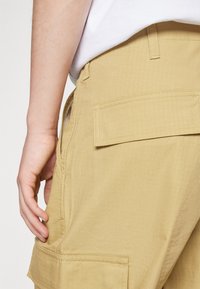 Khaki cargo shorts i et tekstureret stof, med sidelommer og en baglomme med klap. Har synlig syning og en lige skæring.