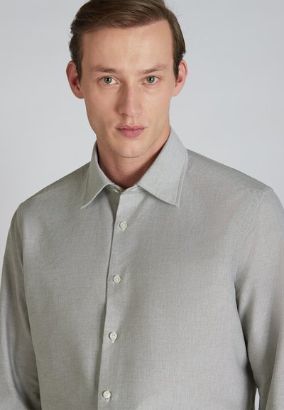 Camisa gris de botones con un acabado texturizado, que presenta un collar puntiagudo y botones blancos, llevada por un modelo con un fondo neutro.