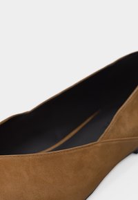 Chaussure plate en daim marron à bout pointu avec un petit talon et une doublure intérieure noire sur un fond blanc uni.