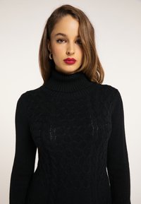 Maglione nero a maglia con colletto alto a coste, caratterizzato da un motivo a trecce testurizzato e maniche lunghe. Il materiale appare morbido e accogliente.