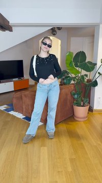 Μαύρο μακρυμάνικο μπλουζάκι με γυάλινες ανταύγειες, ανοιχτό μπλε φαρδιά τζιν παντελόνια, γκρι υποδήματα και μαύρα γυαλιά ηλίου. Εσωτερικός χώρος με φυτά και έπιπλα.