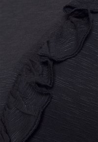 Svart tyg med en texturerad yta och subtil lyster. Har en volangkant längs ena sidan för en accent.