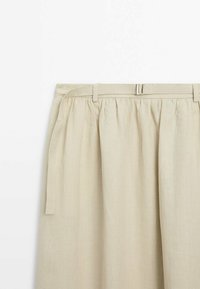 Jupe beige avec taille froncée et fine ceinture en tissu assorti avec une petite boucle métallique sur fond blanc.
