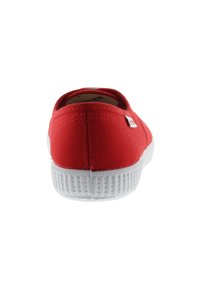 Zapatillas rojas de lona sin cordones con una suela de goma blanca. Textura suave con costuras en la parte trasera y lateral.