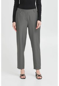 Pantalons gris ajustés avec une texture lisse, coupe droite et poches avant. Les pantalons sont portés avec des sandales noires à lanières.