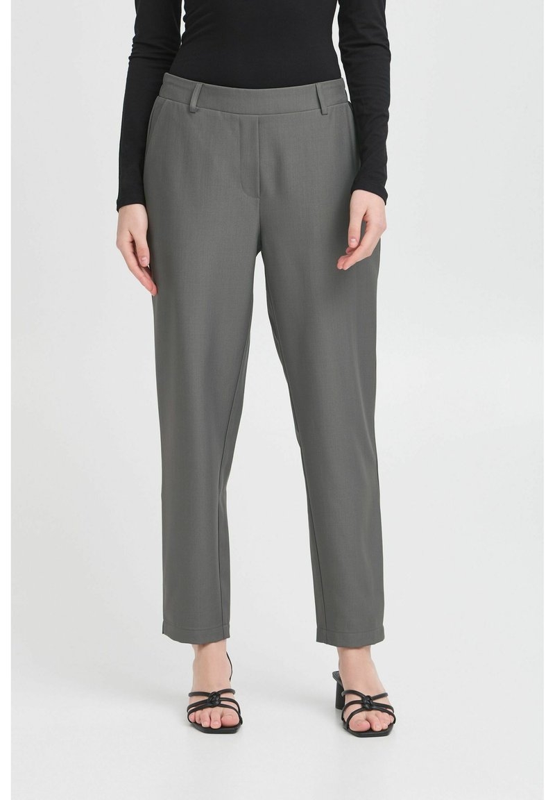 Pantalons gris ajustés avec une texture lisse, coupe droite et poches avant. Les pantalons sont portés avec des sandales noires à lanières.