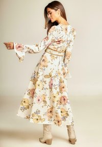 Vestido maxi floral en crema, con flores en tonos pastel, largas mangas acampanadas, cintura ceñida con un cinturón decorativo y tejido texturizado.