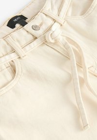 Pantalones color crema de tejido texturizado, con una cintura atada, un botón en la parte delantera y detalles de costura en contraste.