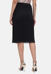 Zwarte geplooide midi-rok met een gladde tailleband, gecombineerd met metallic hoge hakken met een gespsluiting en puntige neuzen.