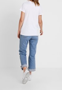 T-shirt bianca in cotone abbinata a jeans di denim azzurro chiaro. I jeans presentano orli arrotolati e una vestibilità dritta, completati da sneaker bianche.