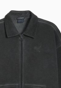 Sort zip-jakke med en blød tekstur, stor krave, sidelommer og et diskret logo prægede på brystet. Glat stoffinish.