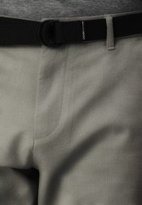 Pantalon gris clair avec une finition texturée, doté d'une ceinture tissée noire et de détails de couture subtils sur les poches.