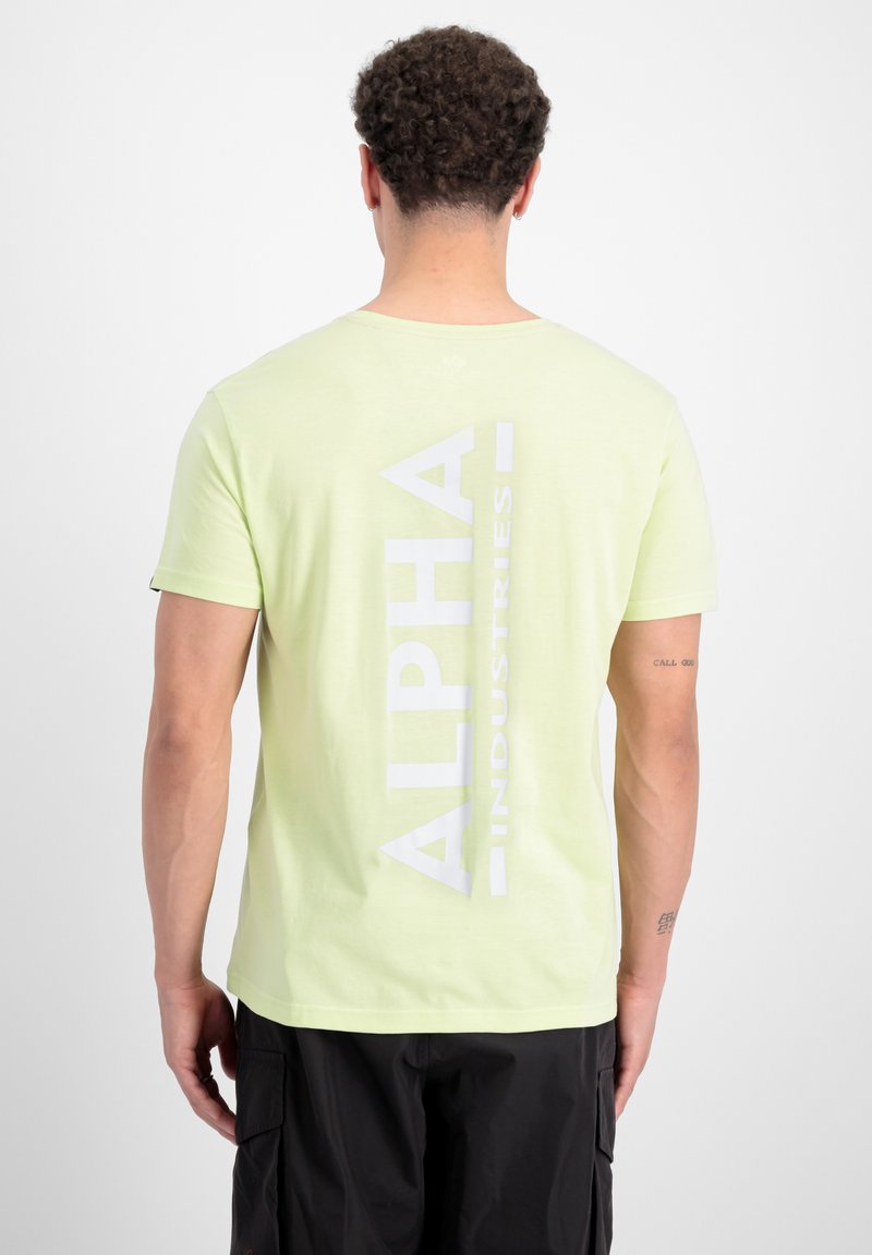 Svijetlozelena majica s kratkim rukavima s velikim bijelim natpisom "ALPHA INDUSTRIES" na leđima. Izrađena je od mekanog, teksturiranog pamučnog materijala.