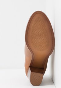 Suola di scarpa in pelle marrone con superficie antiscivolo testurizzata, caratterizzata da un tacco impilato con bordo geometrico e dettaglio di cucitura lungo il lato.