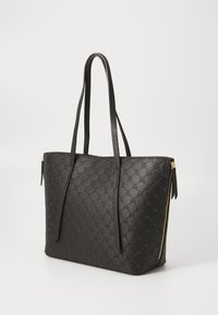 Sac fourre-tout en cuir noir avec motif gaufré, deux longues anses, fermeture éclair et détails en métal doré. Texture lisse et forme structurée.