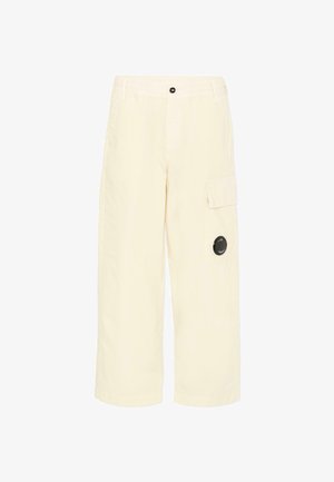 Kremowe szerokie spodnie cargo z przodu na guziki, z klapką boczną, szlufkami na pasek oraz okrągłą czarną naszywką na prawej nogawce.