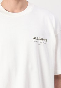 Hvid t-shirt med rund hals med "ALLSAINTS"-logo og japanske tegn trykt på venstre bryst over ordet "LONDON".