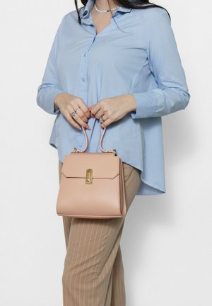 Structured handbag in soft pink leather with a top handle and a gold clasp. Worn with a light blue button-up shirt and tan striped trousers.